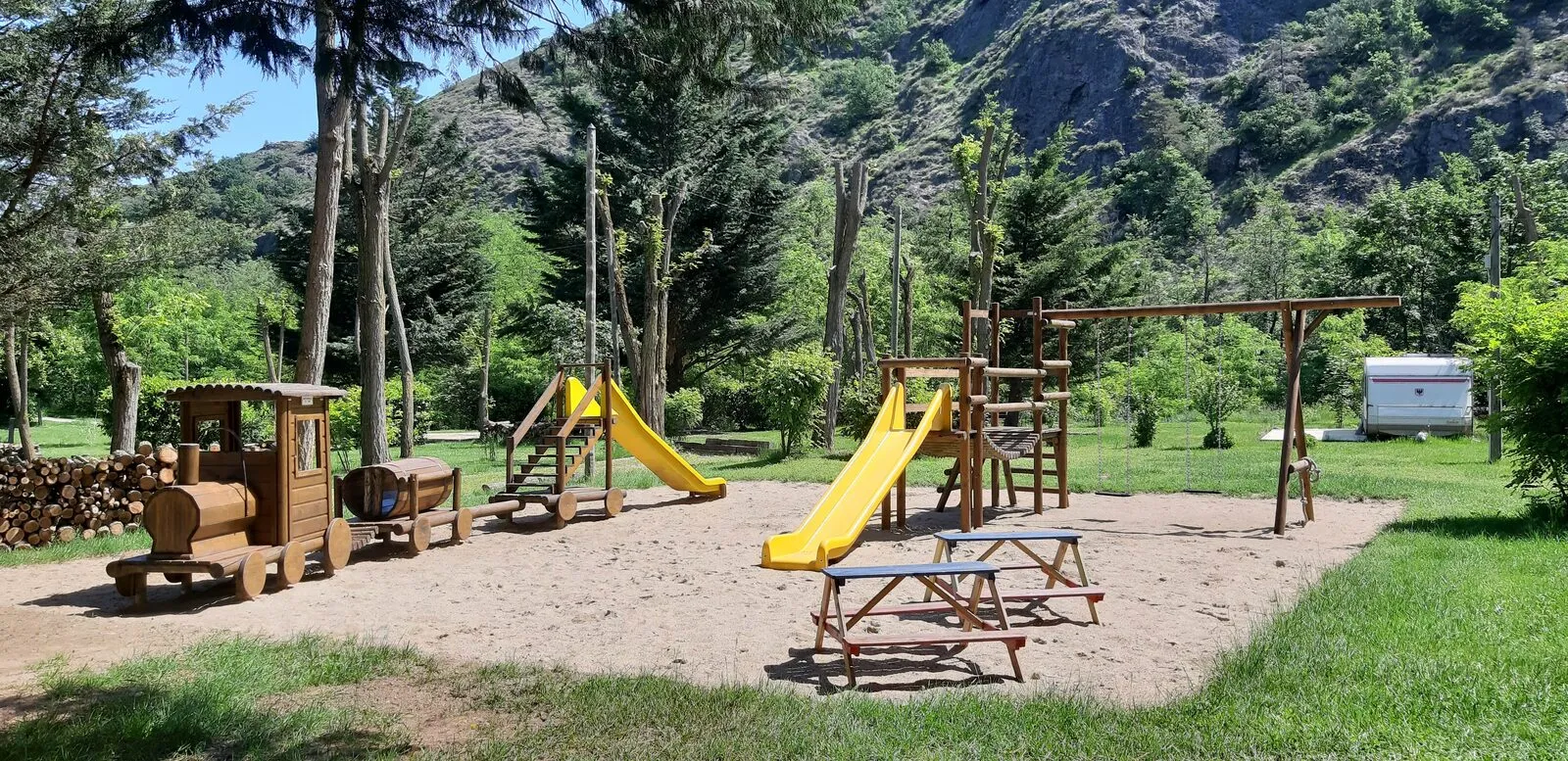 Der Holzspielplatz: die kleine Eisenbahn, das Klettergerüst und seine gelben Rutschen