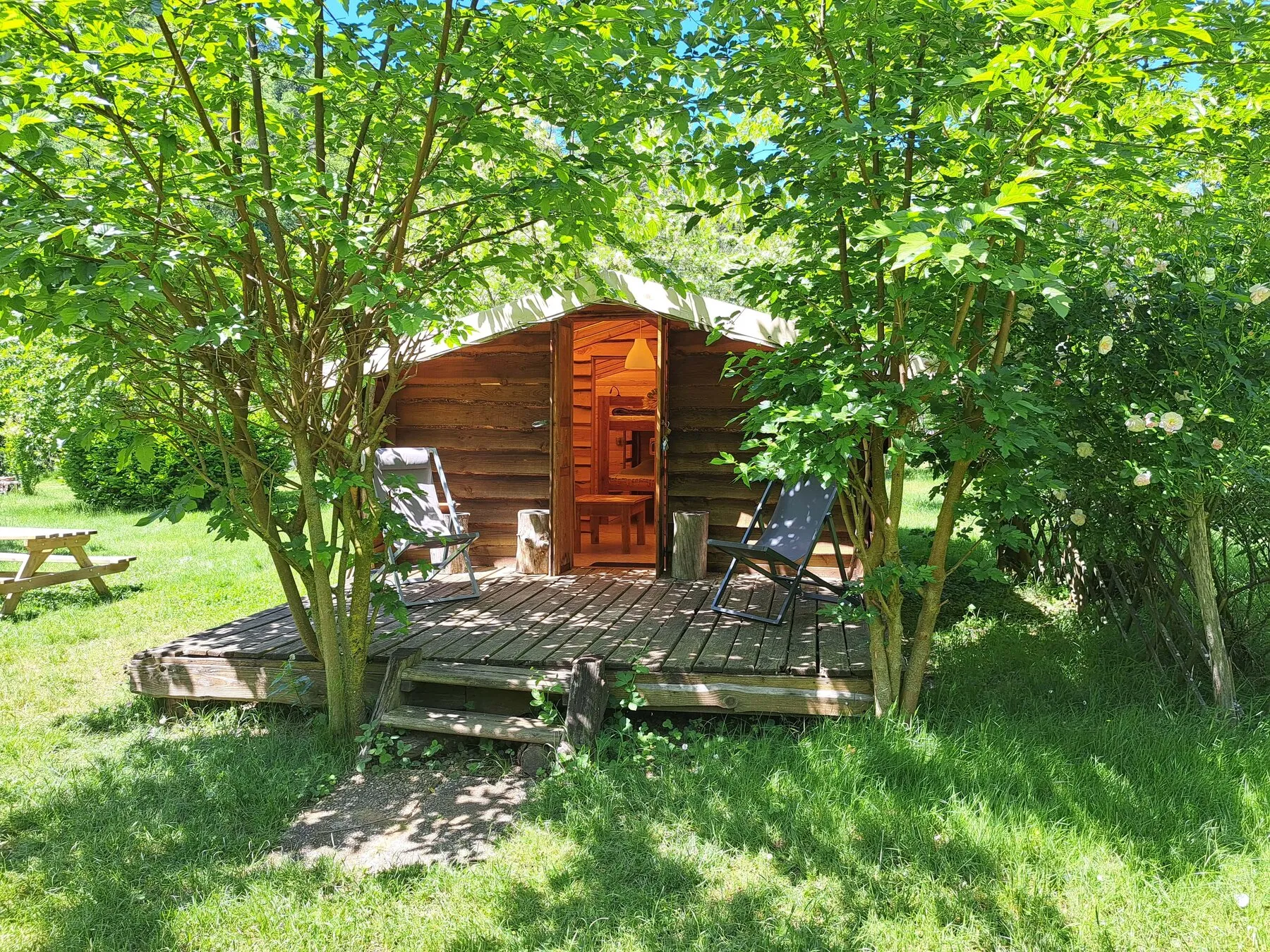 Die Trapperhütte und ihre Holzterrasse, im Schatten der Bäume