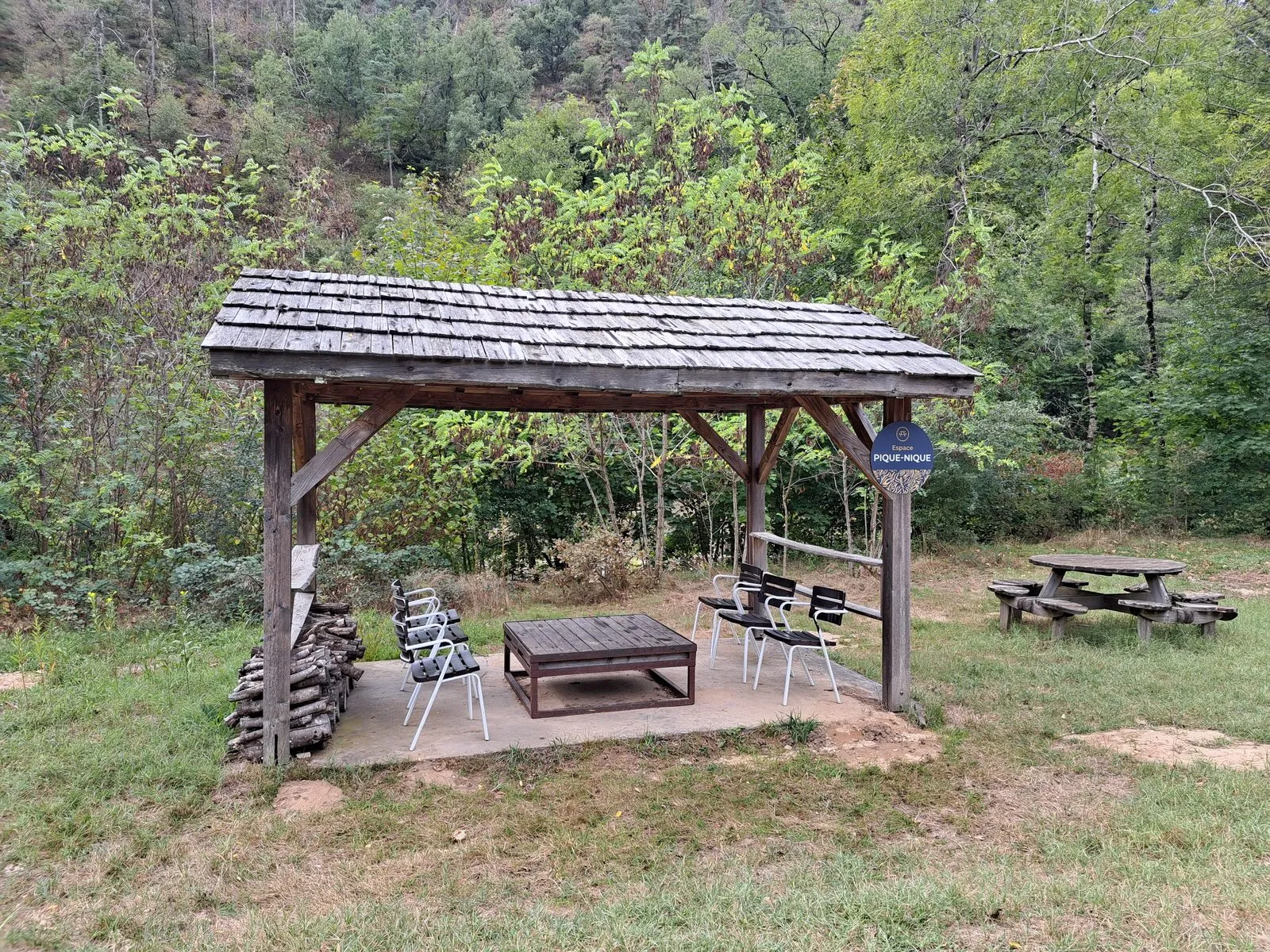 Der Picknickplatz: ein Holzunterstand mit niedrigem Tisch und Stühlen, dazu ein Picknicktisch auf der Wiese