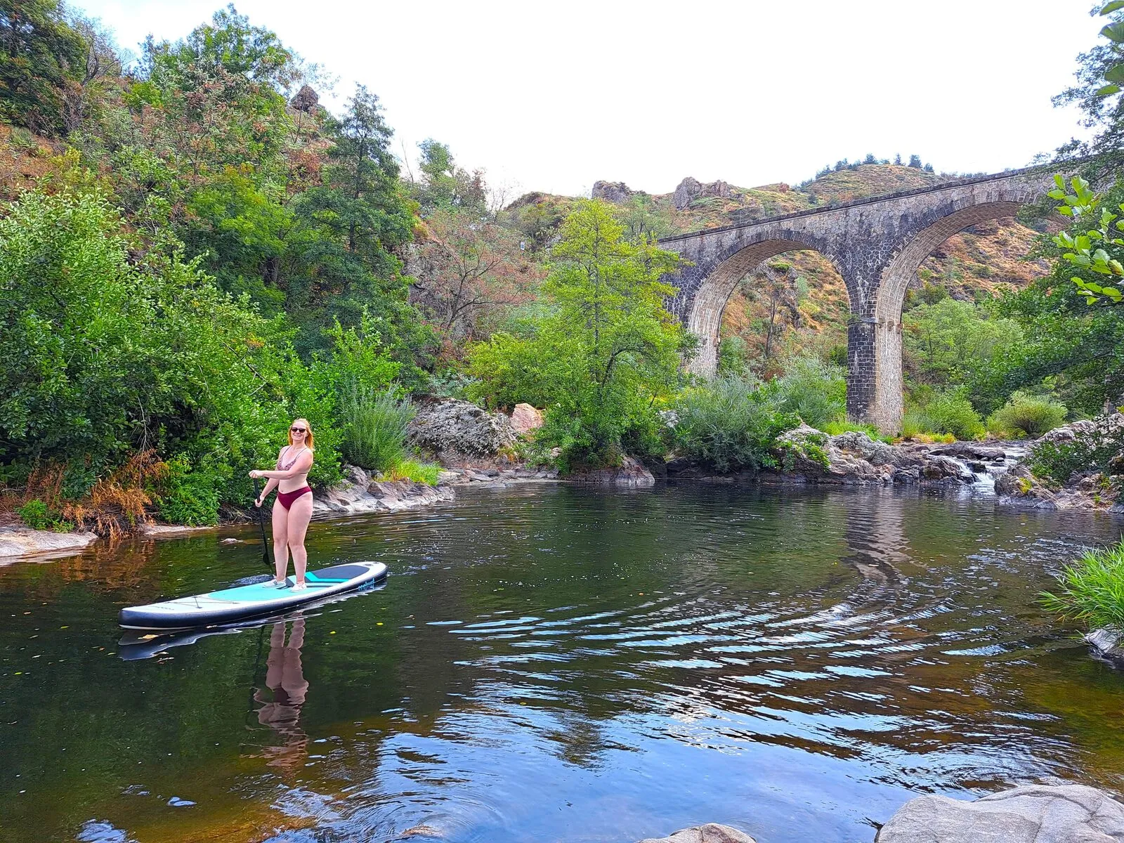 Eine Frau beim Stand-up-Paddling auf dem Doux, vor dem Viadukt