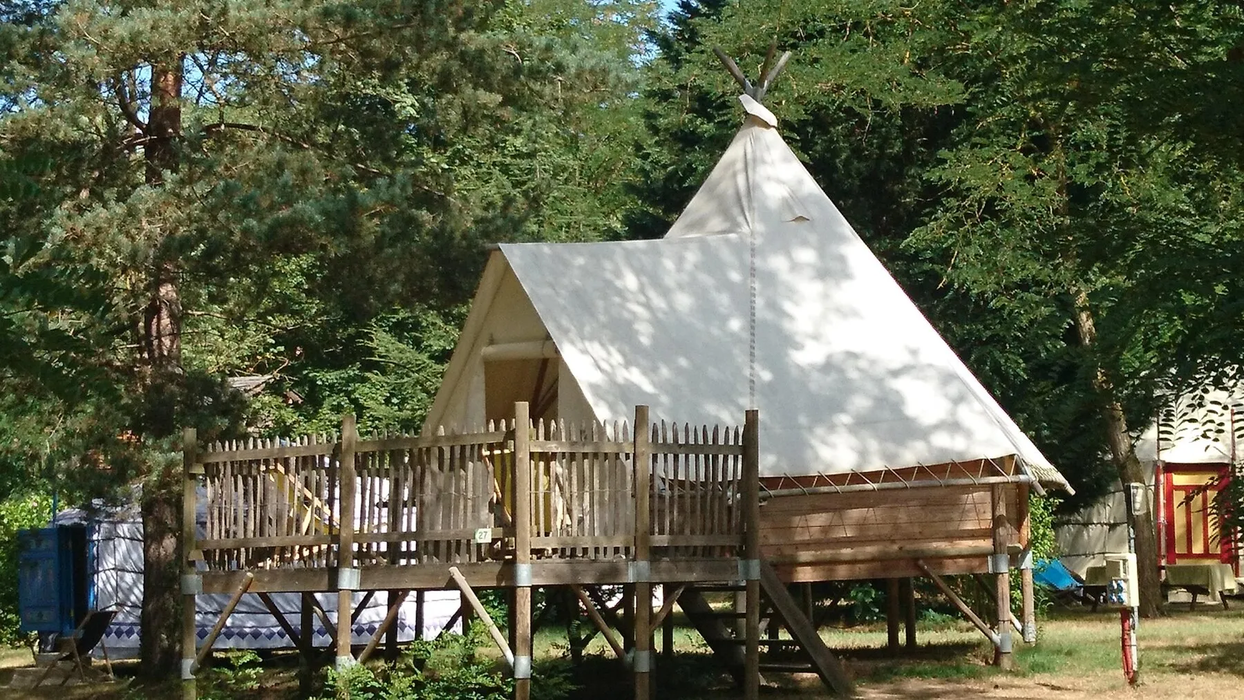 Eine Tipi-Hütte auf ihrer Plattform, im Schatten der Bäume